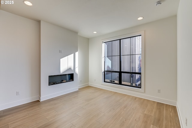 unfurnished living room with baseboards, light wood finished floors, a glass covered fireplace, and recessed lighting