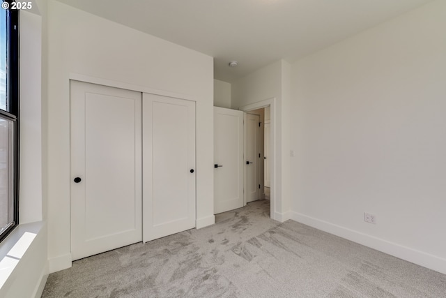 unfurnished bedroom with baseboards, a closet, and light colored carpet