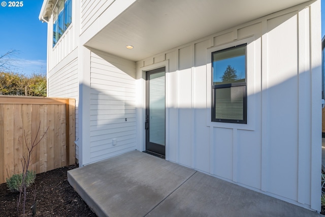 property entrance with board and batten siding, a patio area, and fence