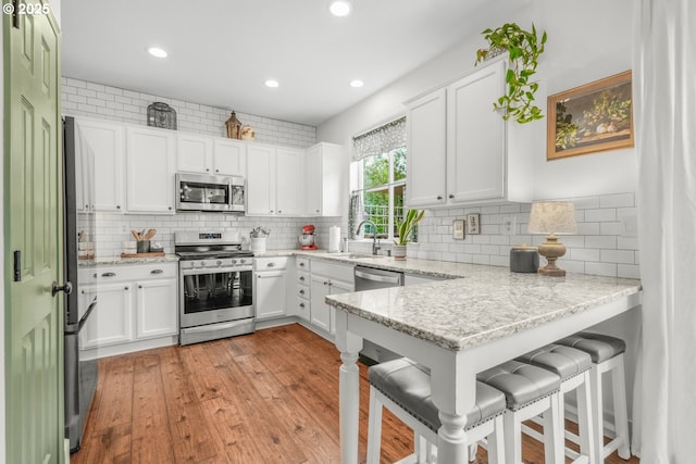 966 NW Brookhill St, Hillsboro, OR 97124 - kitchen with stainless steel appliances, a sink, a peninsula, white cabinets, and light wood-style floors