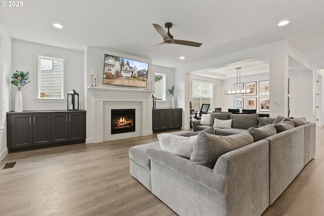 15955 SE Cherry Blossom Way, Happy Valley, OR 97015 - living room featuring light wood-style floors, recessed lighting, ceiling fan, a warm lit fireplace, and healthy amount of natural light
