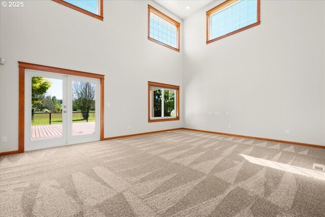 empty room with carpet floors, baseboards, a high ceiling, and french doors