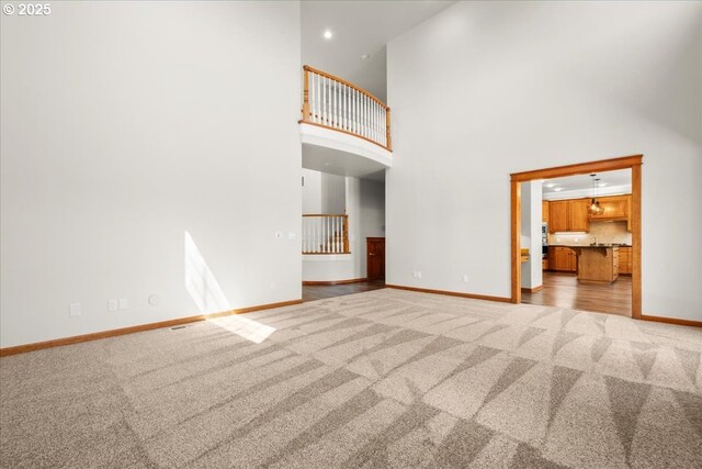 unfurnished living room featuring carpet, baseboards, a towering ceiling, and recessed lighting