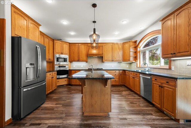 kitchen with appliances with stainless steel finishes, dark stone counters, a center island with sink, dark wood-style floors, and recessed lighting
