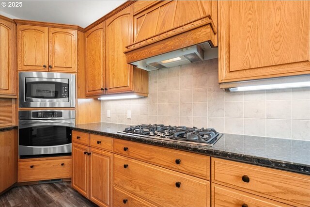 kitchen featuring stainless steel appliances, premium range hood, dark stone countertops, and dark wood-type flooring
