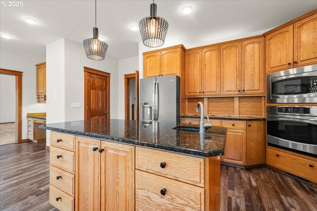 kitchen with appliances with stainless steel finishes, a sink, dark wood finished floors, dark stone countertops, and pendant lighting