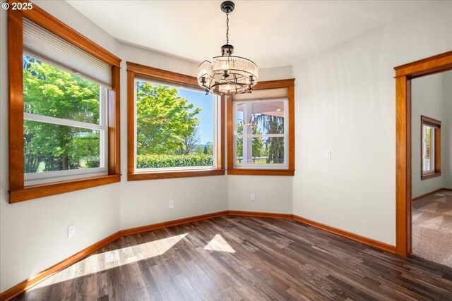 unfurnished room featuring a chandelier, wood finished floors, and baseboards
