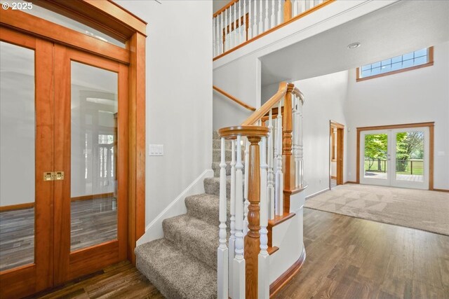 stairs featuring wood finished floors, a towering ceiling, french doors, and baseboards