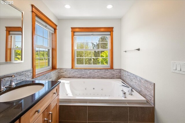 full bathroom with healthy amount of natural light, a tub with jets, vanity, and recessed lighting