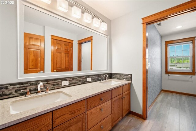 full bath featuring wood finished floors, decorative backsplash, baseboards, and double vanity