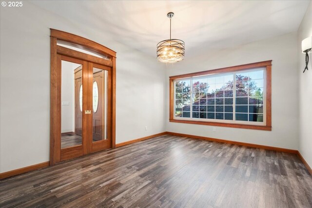 spare room featuring baseboards, dark wood-type flooring, and a chandelier