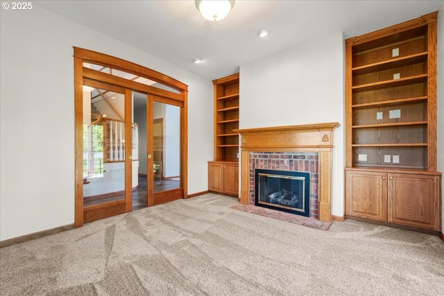 unfurnished living room with carpet floors, baseboards, a brick fireplace, built in features, and french doors