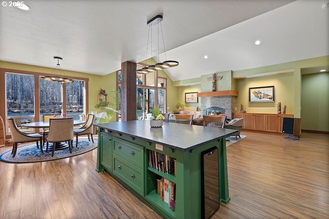 kitchen featuring green cabinetry, a fireplace, wood finished floors, pendant lighting, and vaulted ceiling