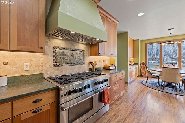 kitchen with wall chimney exhaust hood, double oven range, light wood-style flooring, backsplash, and baseboards