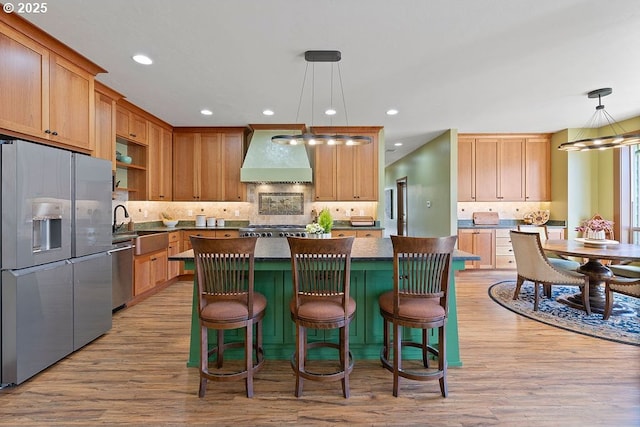 kitchen with appliances with stainless steel finishes, wall chimney exhaust hood, dark countertops, wood finished floors, and backsplash