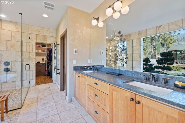 full bath with tile walls, a shower stall, a spacious closet, double vanity, and recessed lighting
