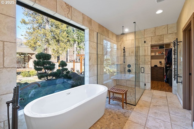full bath featuring tile walls, a shower stall, a freestanding tub, a spacious closet, and stone finish flooring