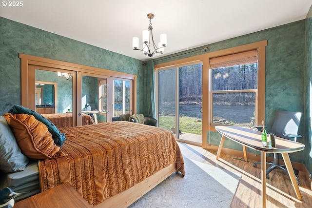 bedroom featuring french doors, access to outside, a chandelier, a water view, and wood finished floors