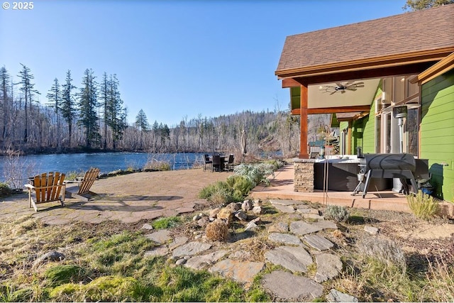 view of yard with a ceiling fan, a water view, a patio area, and a view of trees