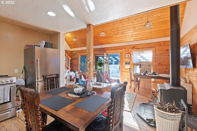 dining space featuring light wood finished floors, a wood stove, wooden walls, and recessed lighting