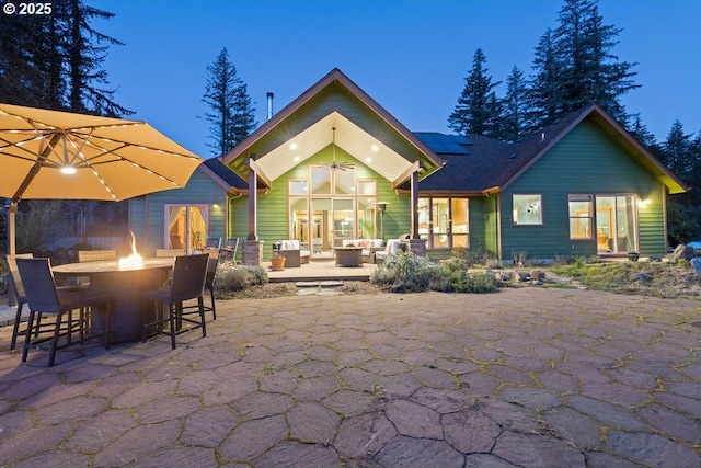 rear view of property with a patio, roof mounted solar panels, an outdoor living space with a fire pit, and ceiling fan