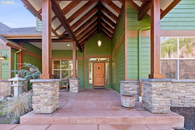 entrance to property with covered porch, roof with shingles, and stone siding