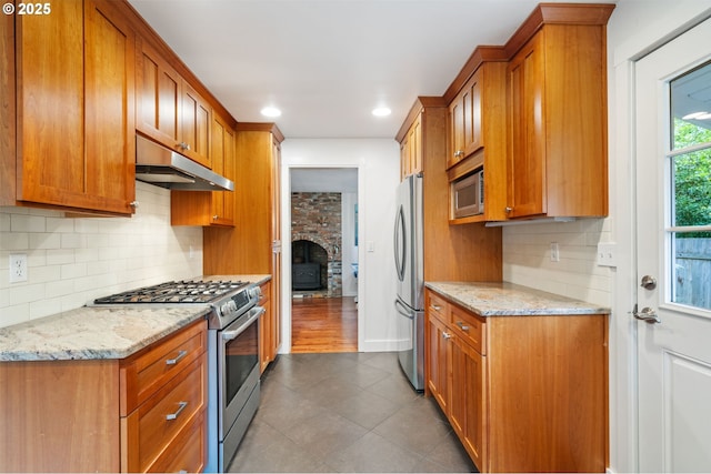 5239 Madrona St, Lake Oswego, OR 97035 - kitchen featuring appliances with stainless steel finishes, under cabinet range hood, brown cabinetry, dark tile patterned floors, and recessed lighting