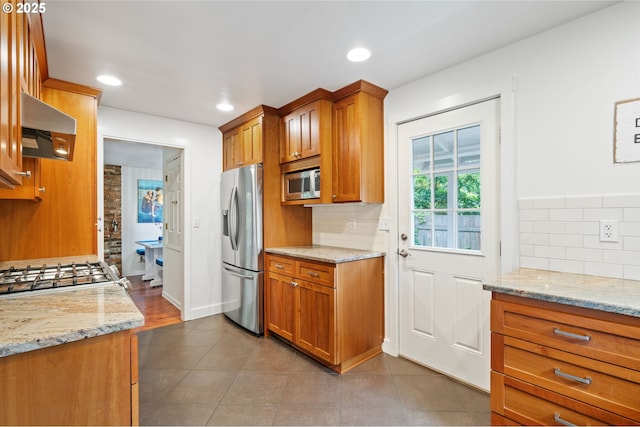5239 Madrona St, Lake Oswego, OR 97035 - kitchen featuring appliances with stainless steel finishes, wall chimney exhaust hood, brown cabinets, backsplash, and light stone countertops
