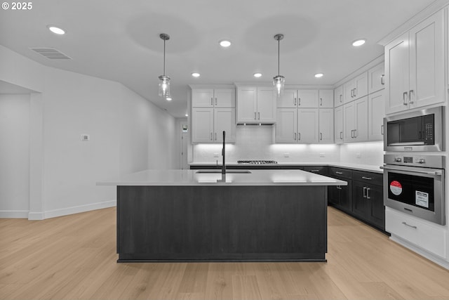 kitchen with white cabinetry, hanging light fixtures, a kitchen island with sink, and stainless steel appliances