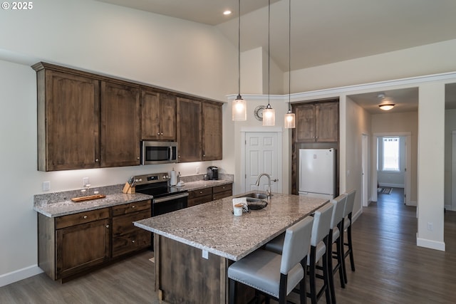 kitchen with dark wood-style flooring, a sink, stainless steel appliances, dark brown cabinetry, and a kitchen breakfast bar