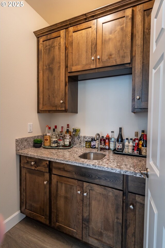 kitchen featuring dark wood-style floors, baseboards, light stone countertops, a sink, and dark brown cabinetry