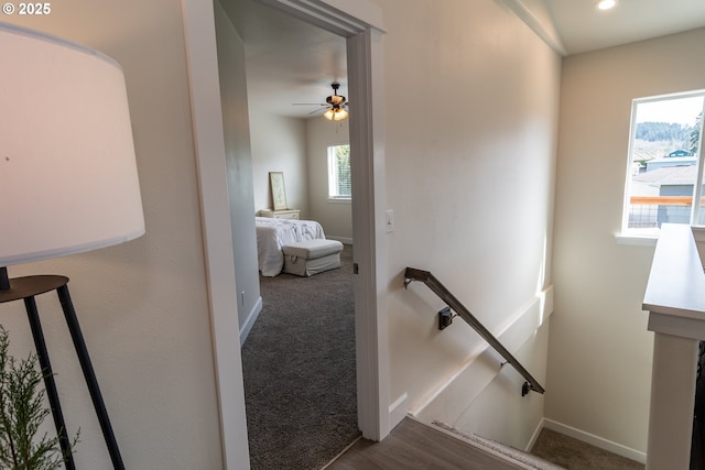 hall featuring baseboards, an upstairs landing, a healthy amount of sunlight, and dark carpet