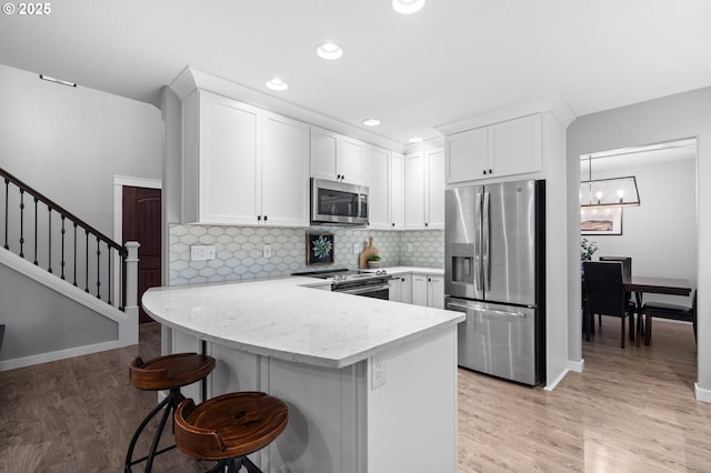 kitchen with stainless steel appliances, light wood-type flooring, a peninsula, and white cabinetry