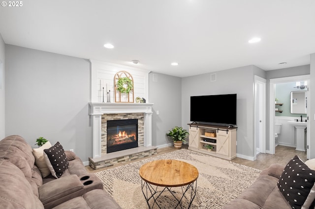 living area featuring light wood-style floors, baseboards, a stone fireplace, and recessed lighting