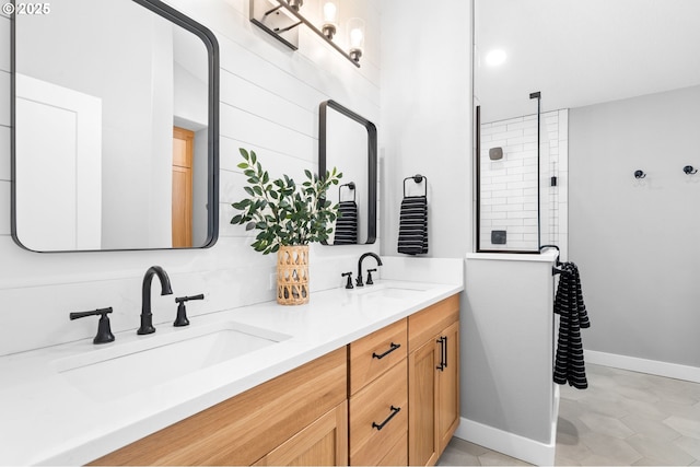 full bath with double vanity, baseboards, a sink, and tiled shower