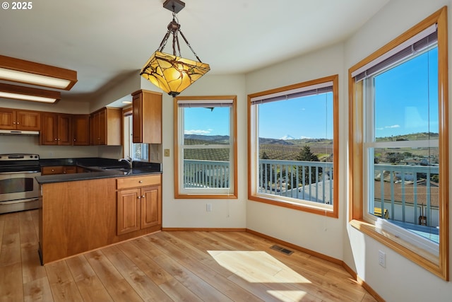 kitchen with brown cabinetry, visible vents, stainless steel electric range, under cabinet range hood, and dark countertops