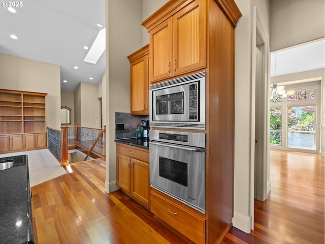 kitchen featuring backsplash, stainless steel appliances, wood-type flooring, an inviting chandelier, and dark stone countertops