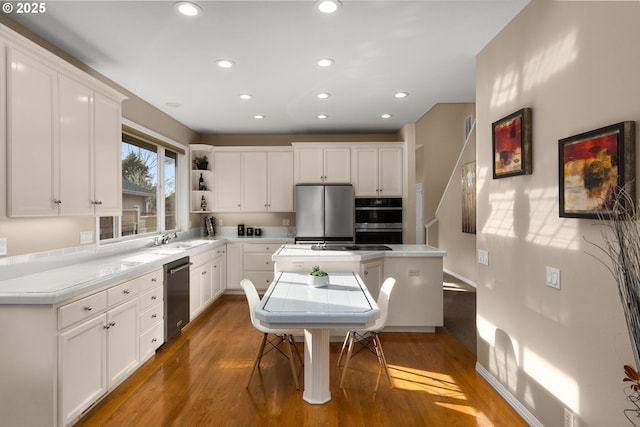 kitchen with recessed lighting, a sink, wood finished floors, white cabinets, and appliances with stainless steel finishes