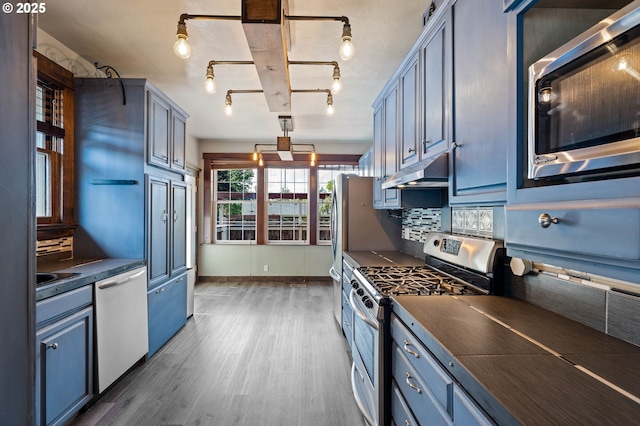 622 C St, Washougal, WA 98671 - kitchen with appliances with stainless steel finishes, dark countertops, under cabinet range hood, wood finished floors, and blue cabinetry