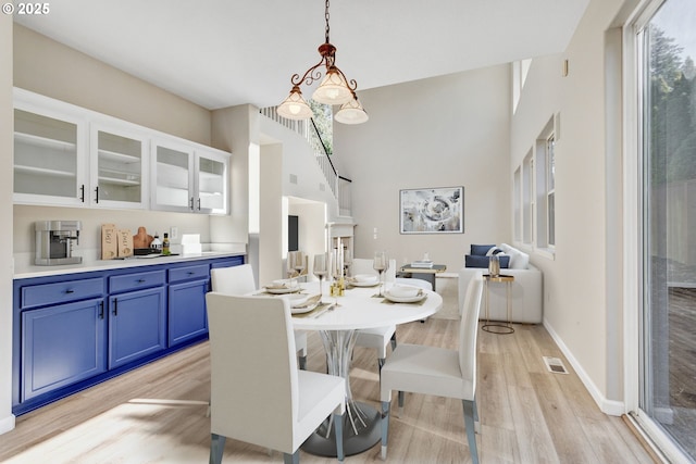 dining area with a towering ceiling, light wood finished floors, baseboards, and visible vents