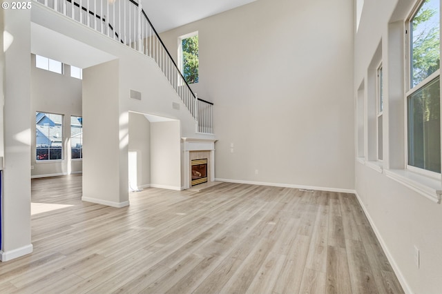 unfurnished living room with baseboards, visible vents, a tile fireplace, wood finished floors, and a high ceiling