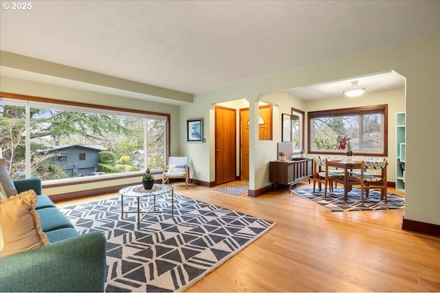 living room with wood finished floors, baseboards, decorative columns, arched walkways, and a textured ceiling