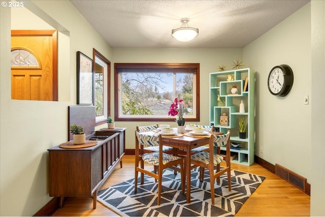 dining room featuring light wood finished floors, visible vents, a textured ceiling, and baseboards