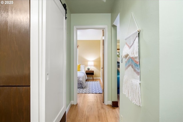 hallway featuring baseboards, light wood-type flooring, and a barn door