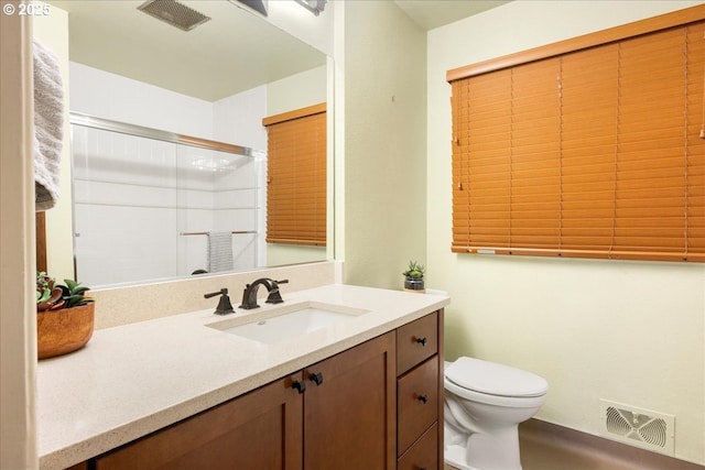 bathroom featuring visible vents, toilet, vanity, and a shower with shower door