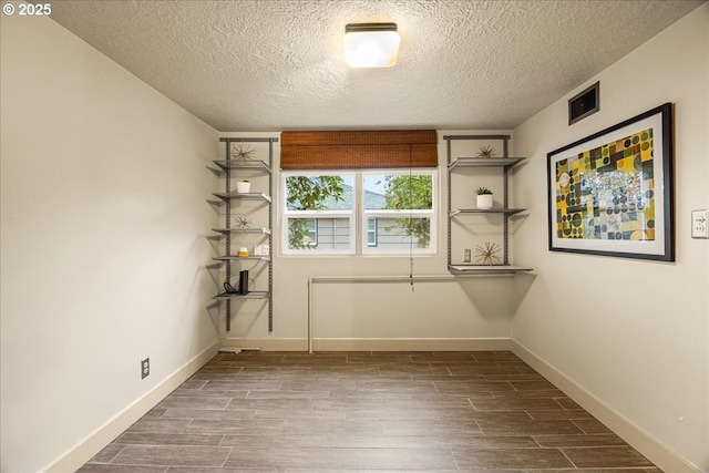 empty room featuring visible vents, a textured ceiling, baseboards, and wood tiled floor