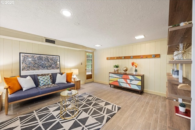 living room featuring wood finish floors, visible vents, baseboards, and a textured ceiling