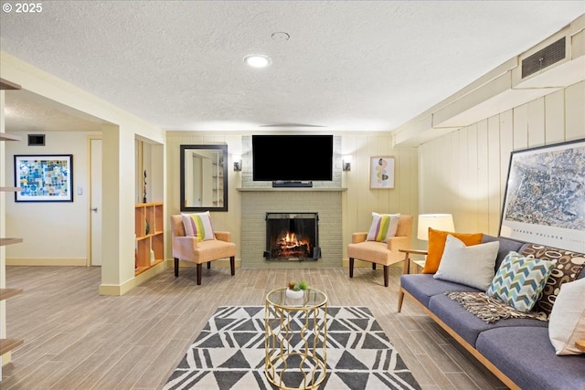 living room with visible vents, a brick fireplace, a textured ceiling, and wood finish floors