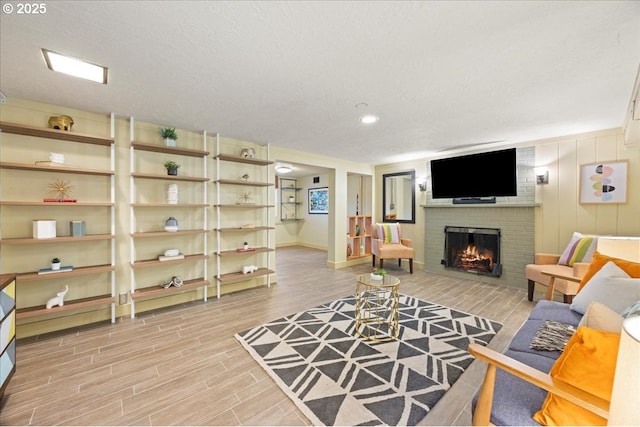 living area with a fireplace, a textured ceiling, light wood-type flooring, and baseboards