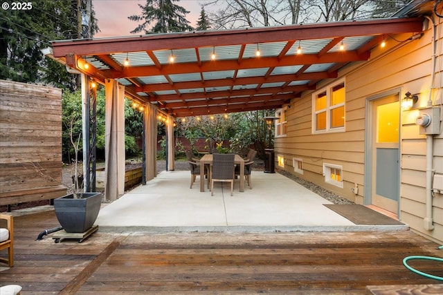 patio terrace at dusk with outdoor dining area, fence, and a wooden deck